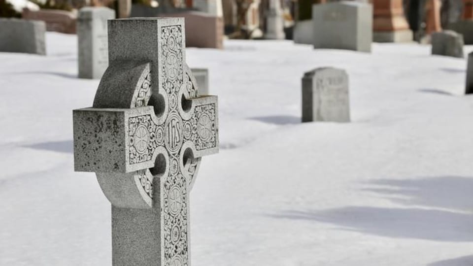 Une croix celtique orne une des tombes du cimetière Saint-Patrick, par une journée d'hiver. On peut apercevoir d'autres tombes derrière. L'endroit respire la paix et le calme. 