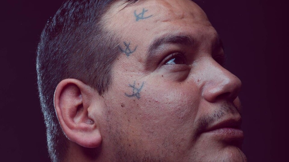 A man posed for a photo with three small bird tattoos on his face.