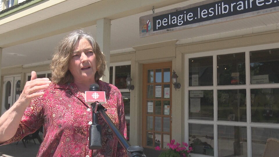 Une femme en entrevue devant un micro de Radio-Canada. La librairie Pélagie et son enseigne sont en arrière-plan.