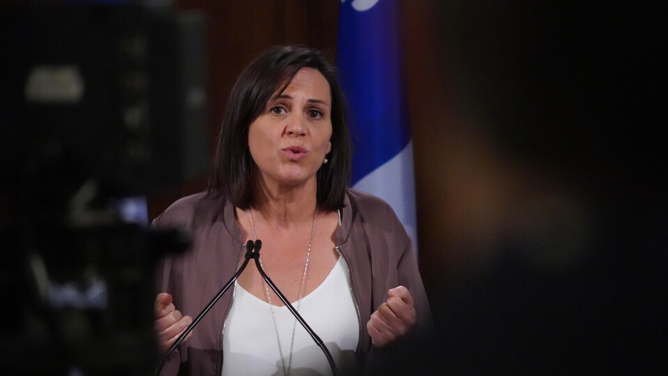 Une femme parle dans un micro devant un drapeau du Québec.
