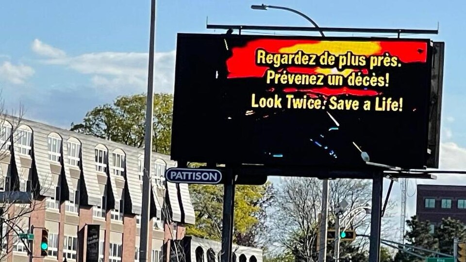Une immense affiche publicitaire au coin d’une rue sur lequel est écrit : Regardez de plus près. Prévenez un décès !
