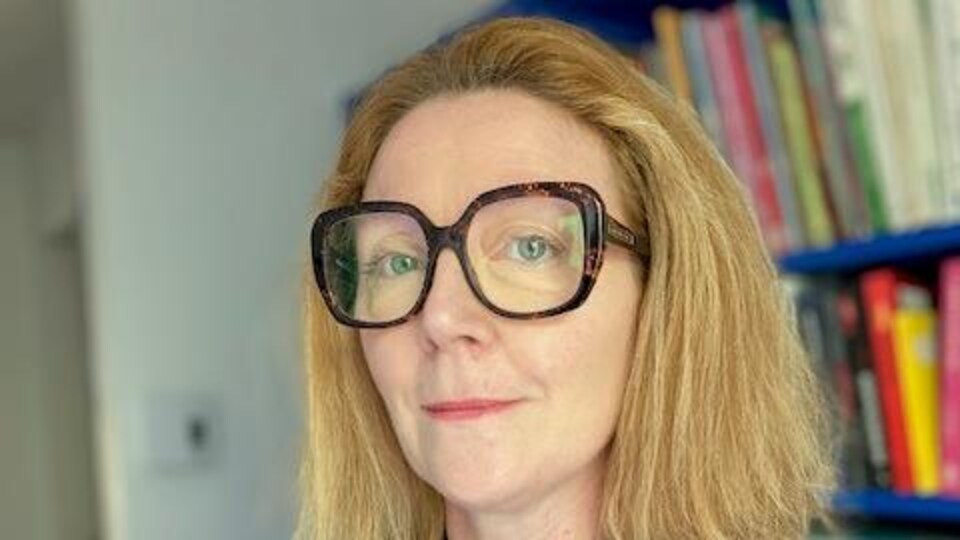 Isabelle Rivoal pose devant une bibliothèque.