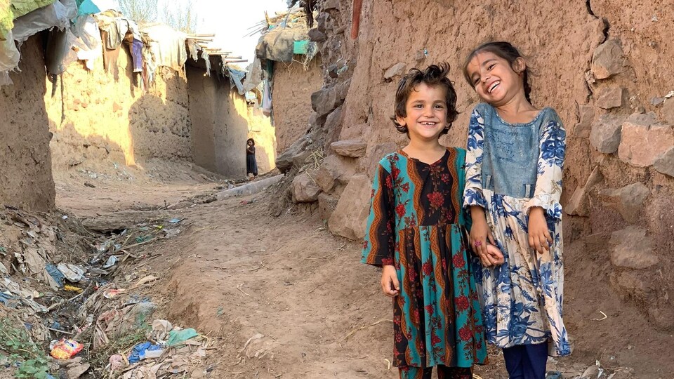 Deux petites filles dans une ruelle de terre bordée de maisons en adobe.