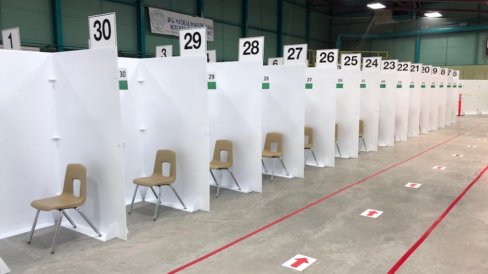 Des chaises sont séparées par des murs en cartons numérotés.