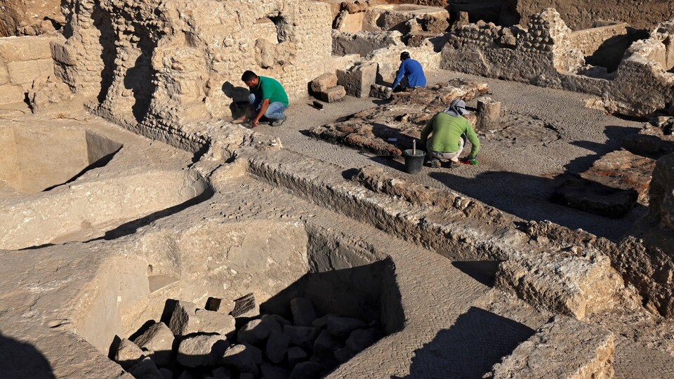 Trois hommes accroupis dans des ruines excavées.