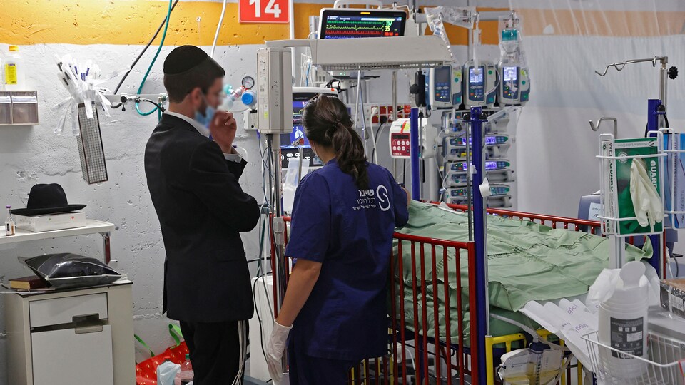 Un homme accompagné d'une soignante regarde son bébé, couché dans un lit. 