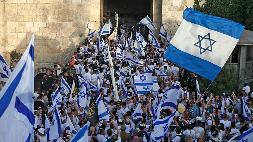 Des centaines de personnes brandissant des drapeaux israéliens devant un mur de pierre. 