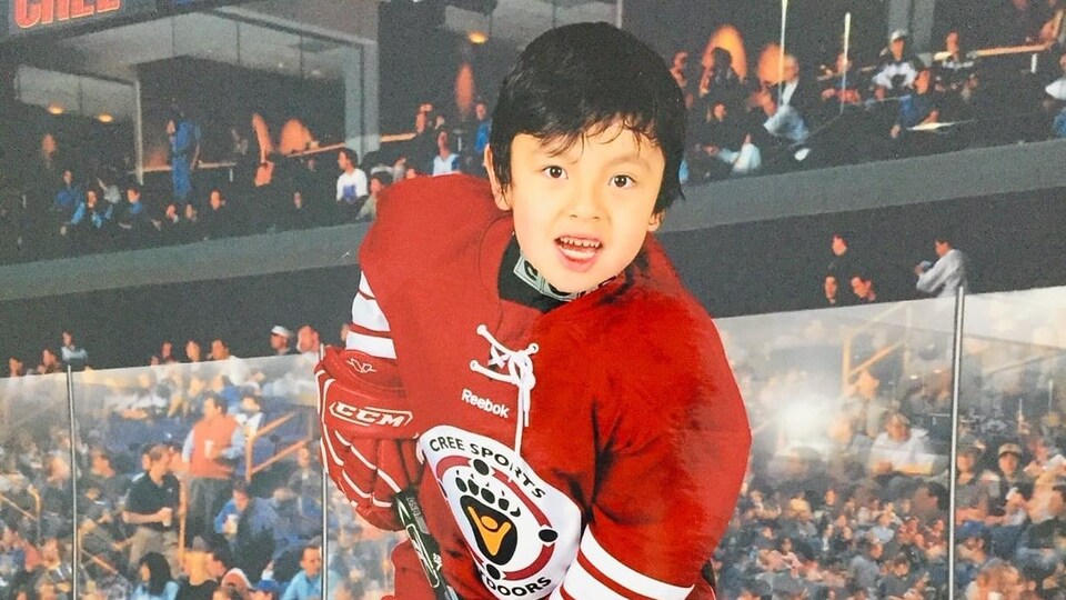 Le garçon pose en équipement de hockey, sur la glace.