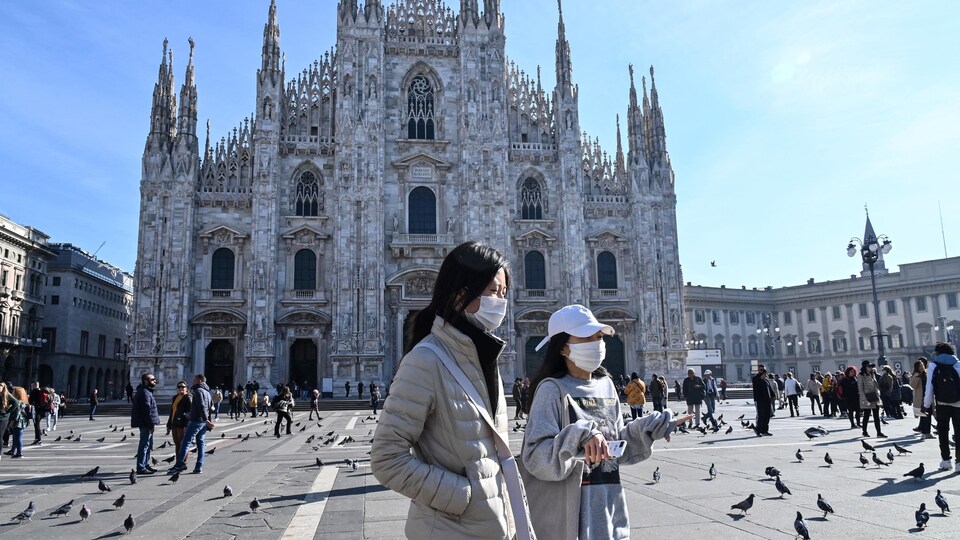 Deux femmes masquées marchent devant la cathédrale de Milan. 