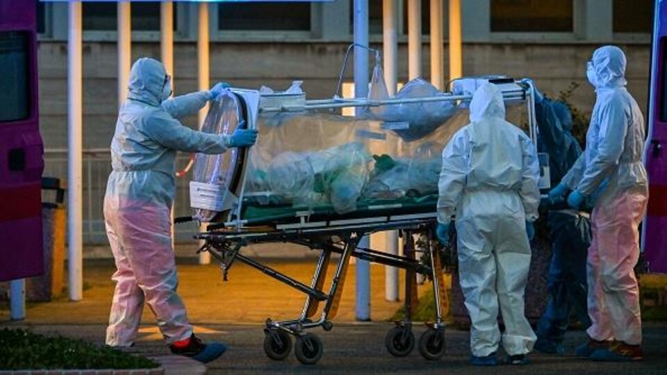 Des travailleurs de la santé en tenue de protection font entrer un patient dans un hôpital.