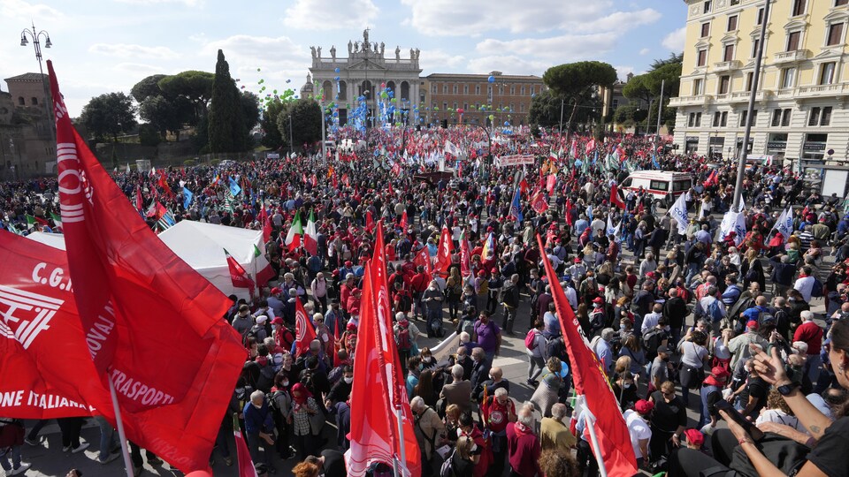 Une foule sur une place de Rome, avec de nombreux drapeaux rouges.