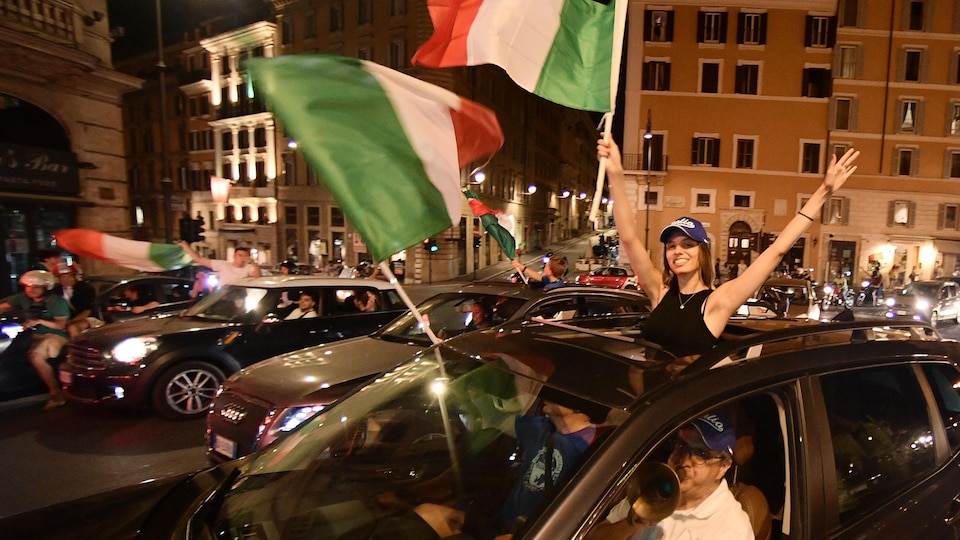 Des partisans agitent des drapeaux italiens hors de leurs voitures.