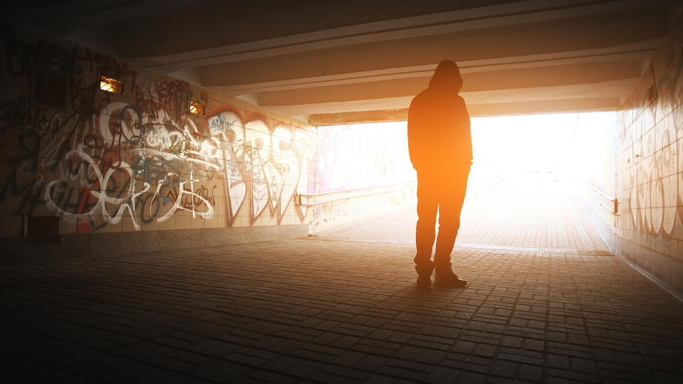 La silhouette d'une personne sous un pont rempli de graffiti.