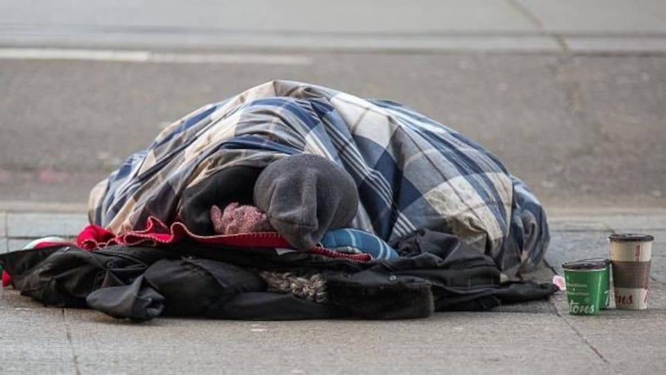 Un homme est couché sur le trottoir sous une grosse couverture.