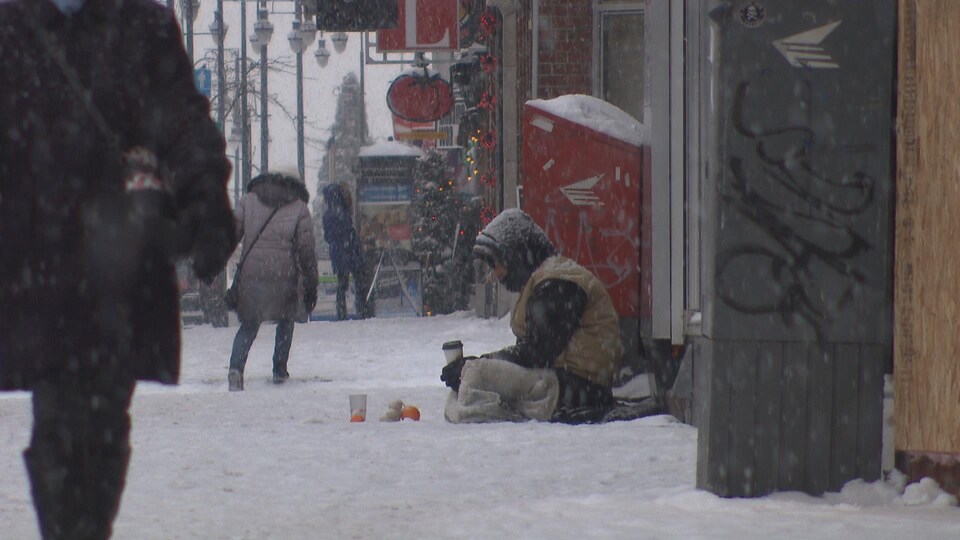 Un homme assis dans la neige sur la rue des Forges en hiver.