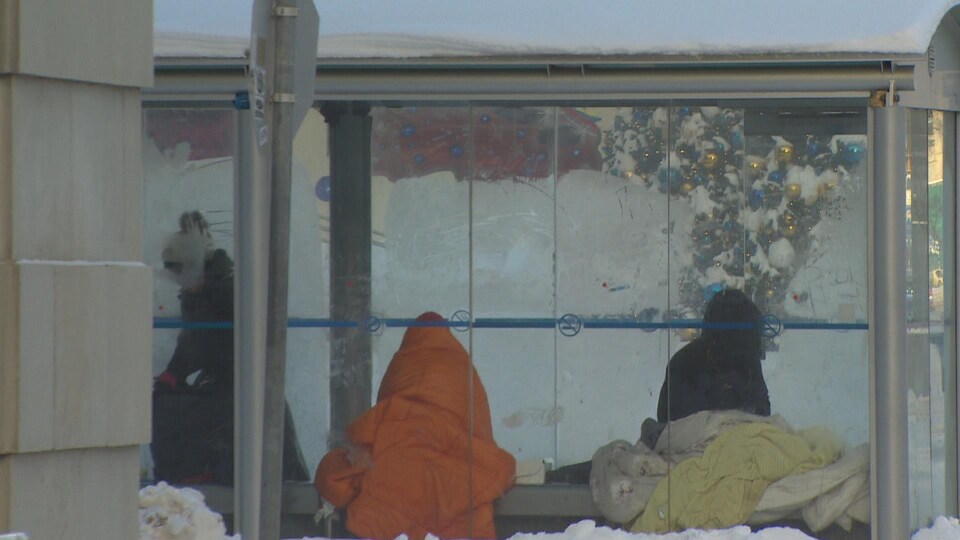 Trois personnes sous des couvertures dans un abribus.