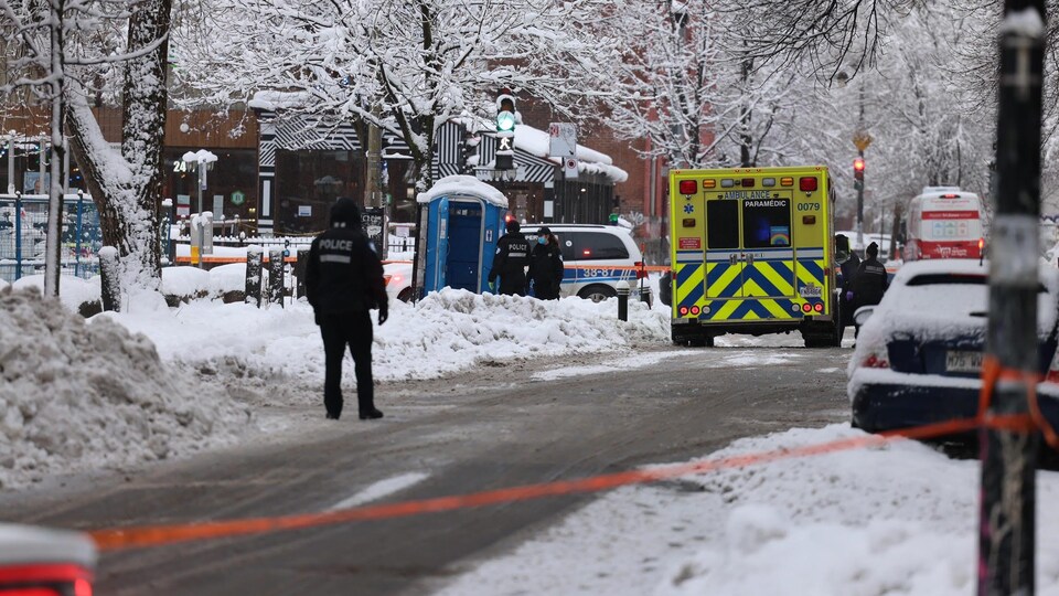 Une ambulance et des policiers près d'une toilette mobile dans une rue enneigée.