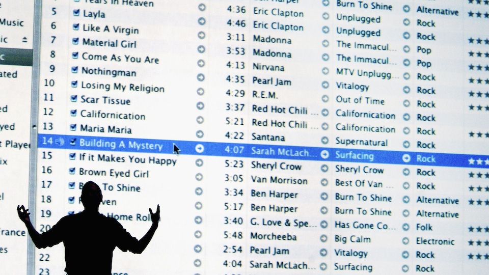 L'ombre d'un homme est visible devant un écran géant présentant une liste de nombreuses chansons disponibles sur une application.