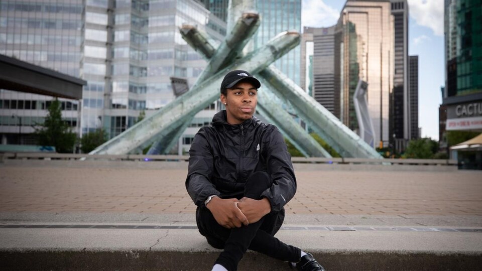 Jacob Callendar Prasad, un jeune homme noir, assis sur un trottoir.