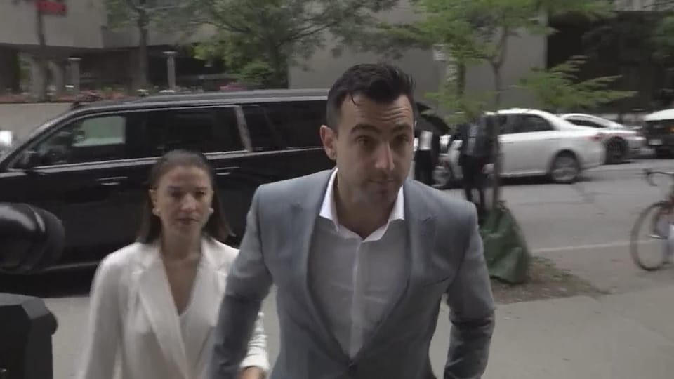 Accompagné de sa femme, le chanteur Jacob Hoggard entre au palais de justice de Toronto, il porte un complet gris clair et une chemise blanche.