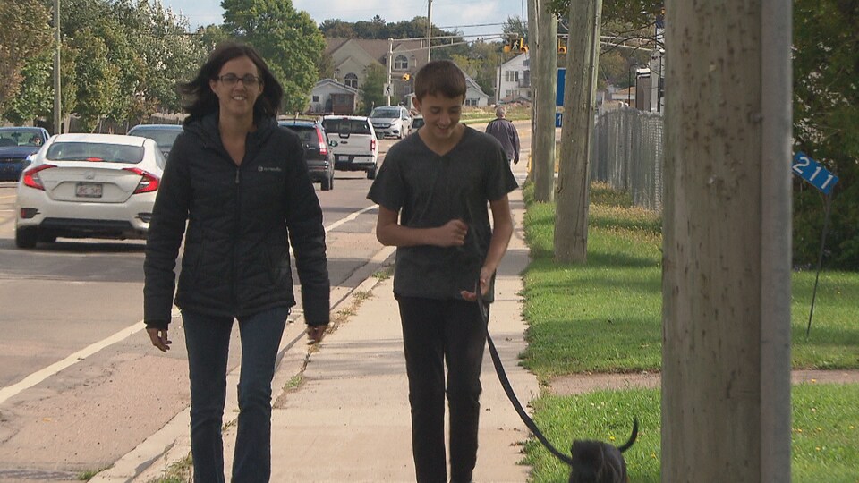 Un adolescent et sa mère marche dans la rue avec un chien. 