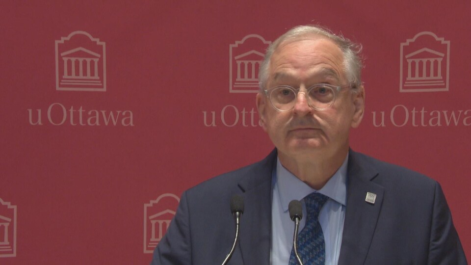 Jacques Frémont s'adresse aux médias devant une bannière aux couleurs de l'Université d'Ottawa.
