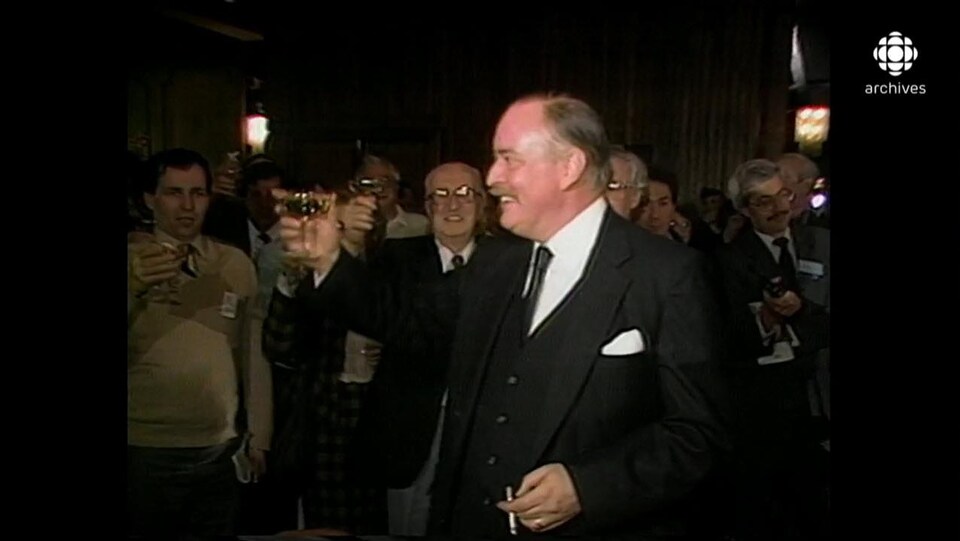 Jacques Parizeau, entouré de militants péquistes, célébrant avec une coupe de champagne à la main et une cigarette dans l'autre.