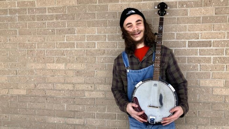 Un jeune homme en salopette souri avec son banjo dans les mains.