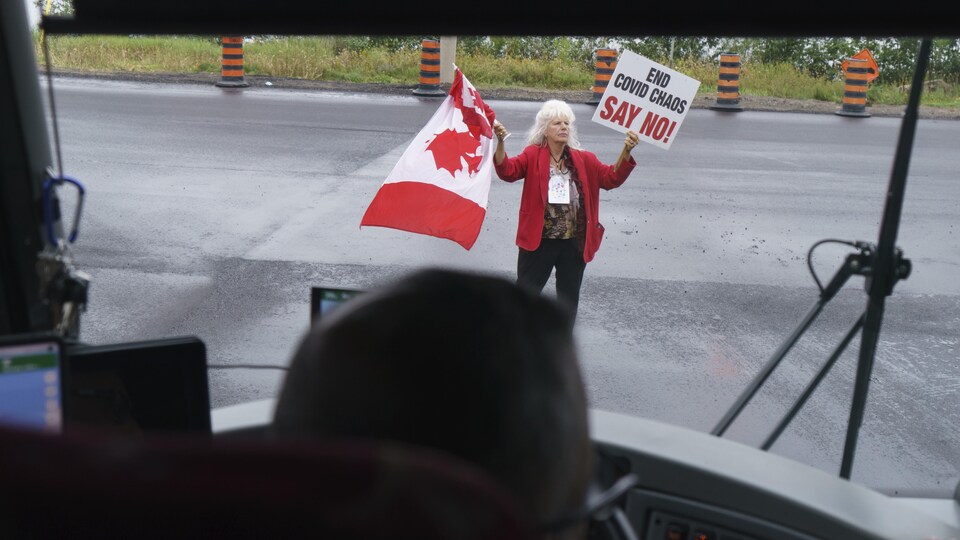 Une femme tenant pancarte et drapeau se tient devant un autobus. 
