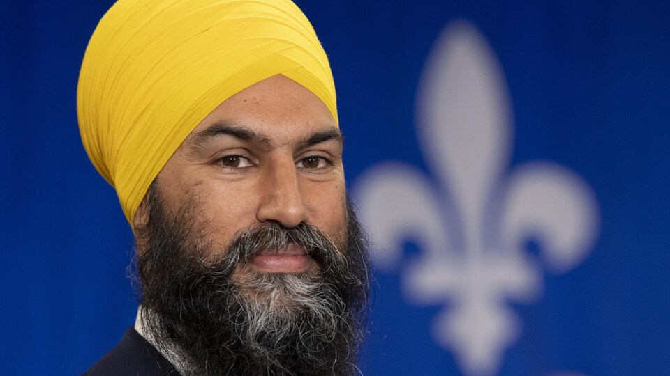 Jagmeet Singh sourit devant un drapeau du Québec.