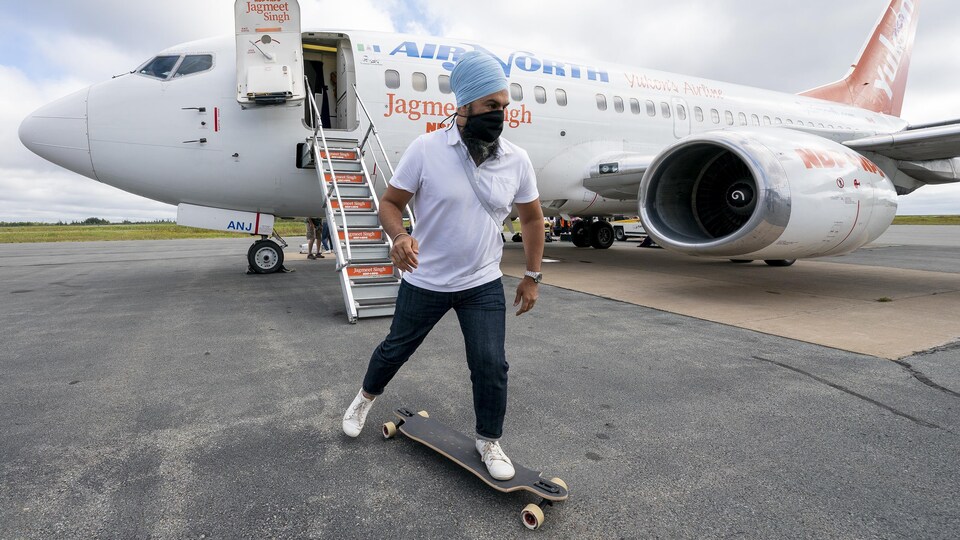 Jagmeet Singh sur un long board devant un avion.