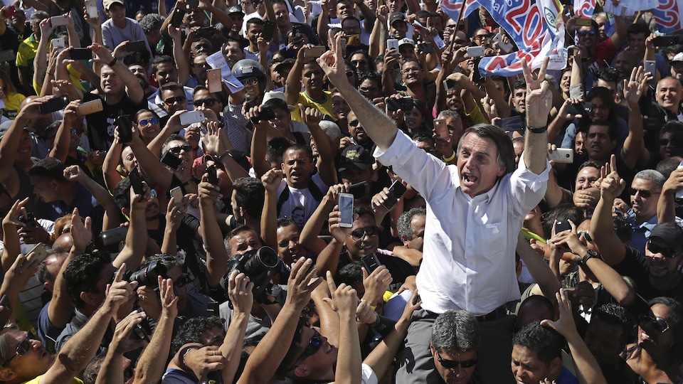 Jair Bolsonaro, candidat à la présidence du Parti national social libéral (NSBP), salue ses partisans alors qu'un membre de son équipe de sécurité le conduit, dans le quartier de Ceilandia, au Brésil, le mercredi 5 septembre 2018.