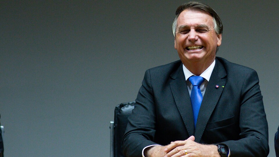 Jair Bolsonaro, assis à une table, sourit.