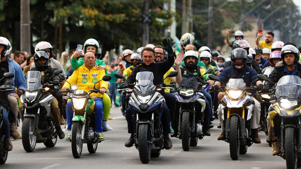 Assis sur une moto à la tête d'un défilé, Jair Bolsonaro salue la foule.