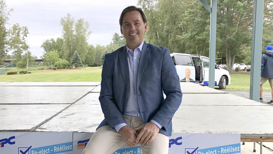 Jake Stewart assis sur le rebord d'une table décorée de ses affiches de campagne électorale.