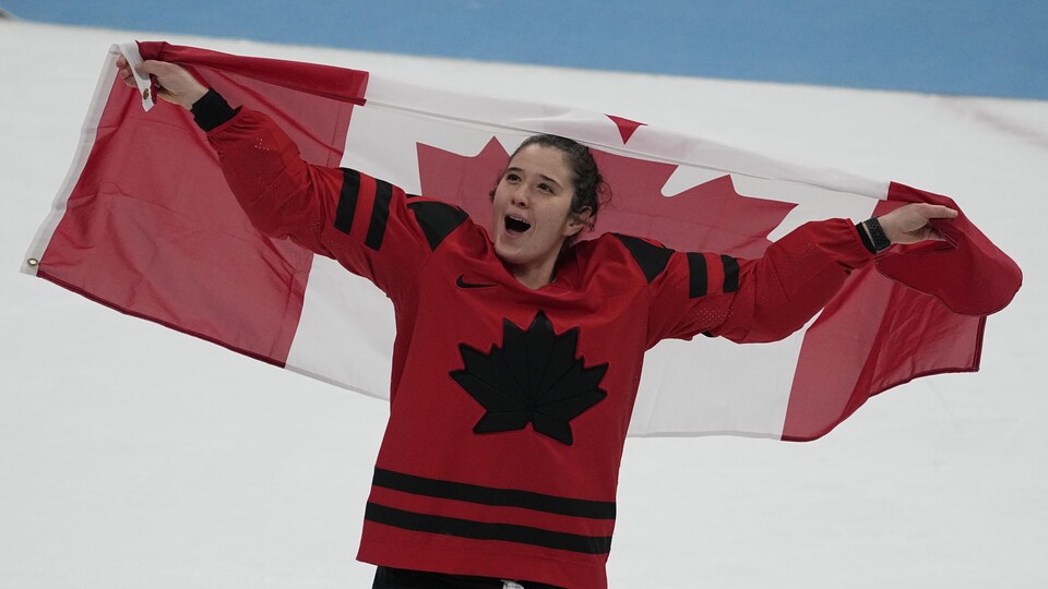 Une hockeyeuse célèbre la victoire sur la glace avec le drapeau canadien.