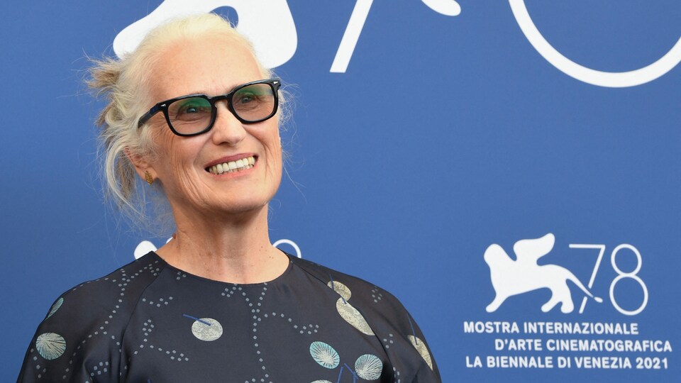 La femme sourit en posant pour les photographes devant un mur bleu avec le logo de la Mostra.