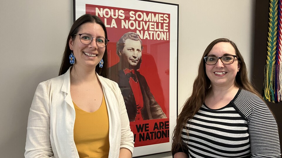 Janelle Delorme et Janet La France devant une affiche avec la photo de Louis Riel et le slogan « Nous sommes la nouvelle nation! »