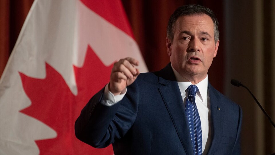 Jason Kenney devant un drapeau du Canada.