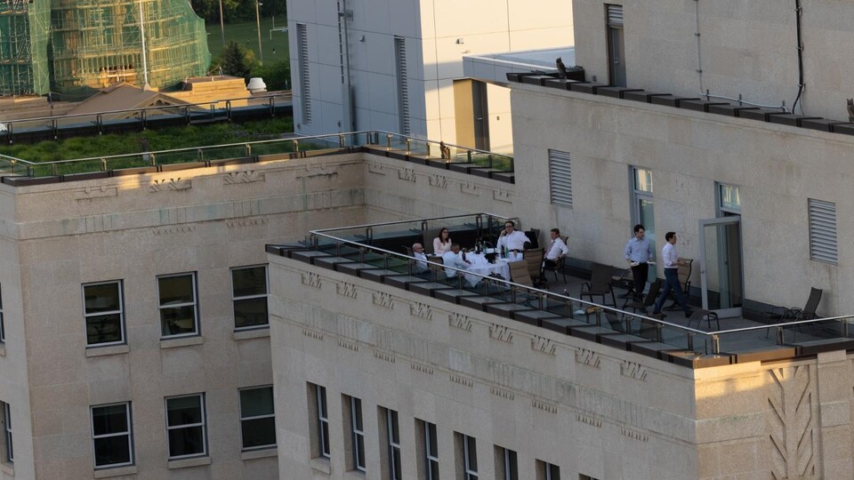 Six personnes mangent à une table ronde sur une terrasse, alors que deux serveurs débarrassent la table.