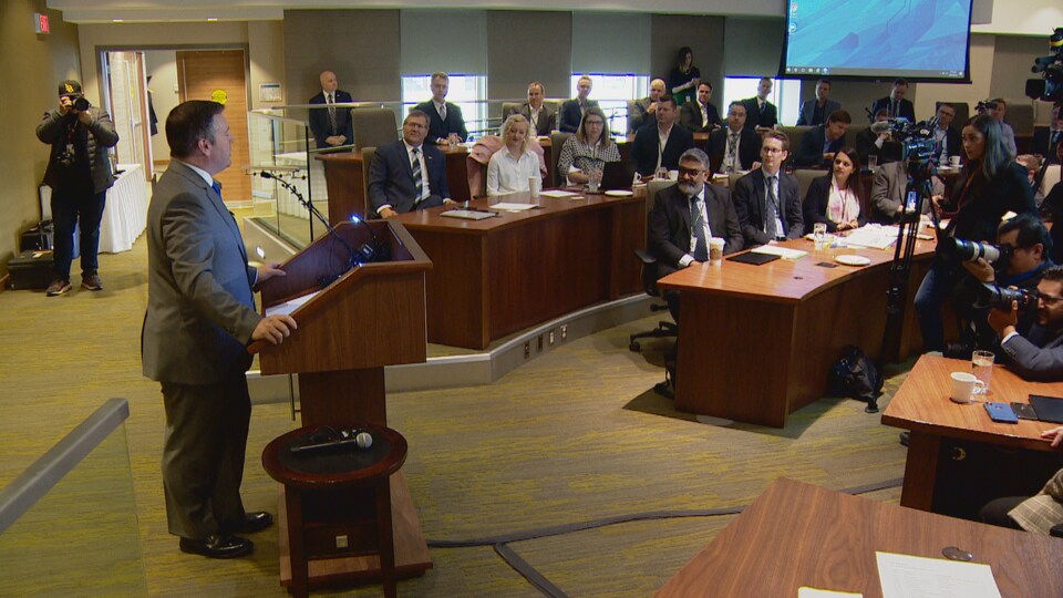 Jason Kenney au pupitre devant le caucus conservateur et des journalistes