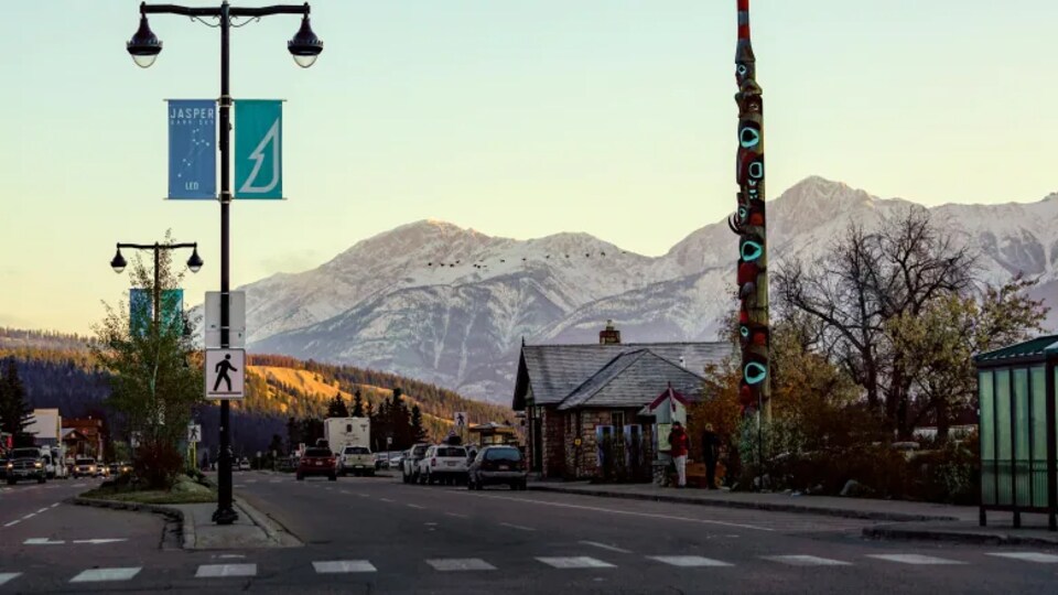 Rue à Jasper avec des voitures stationnées. En arrière-plan, on voit les montagnes Rocheuses.