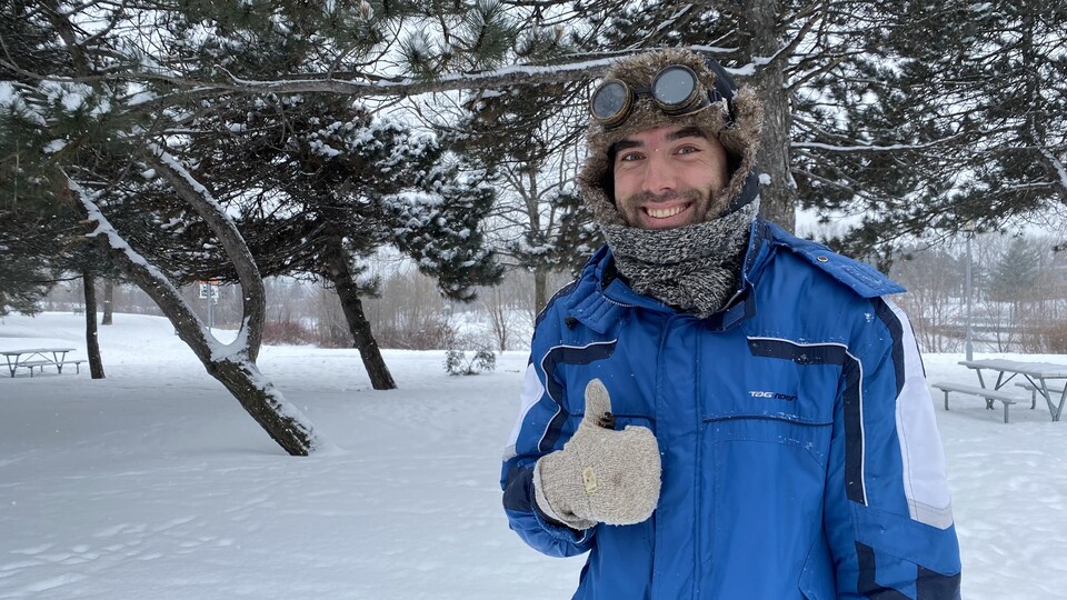 Un homme est habillé en hiver dans un parc et lève le pouce en l'air.