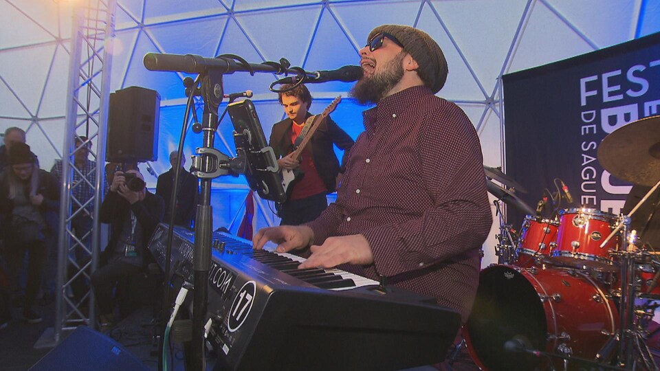 Un homme joue du piano entouré des autres membres de son groupe.