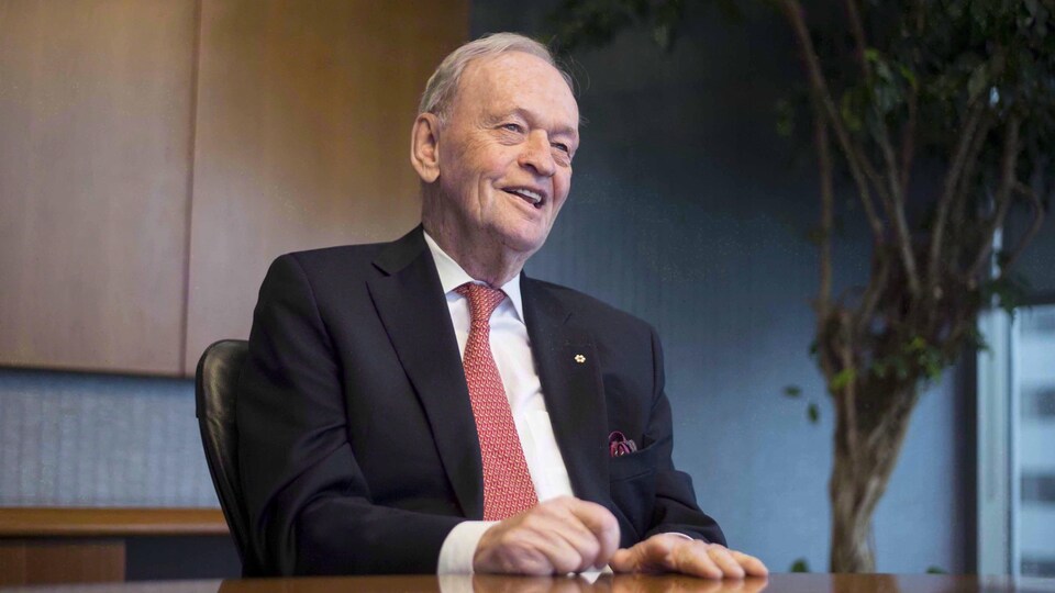 Jean Chrétien est assis derrière une table et sourit.