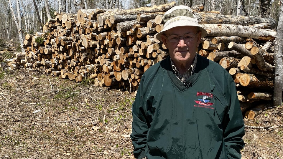 Jean-Guy Comeau se tient debout, les mains dans les poches, devant une corde de bois.