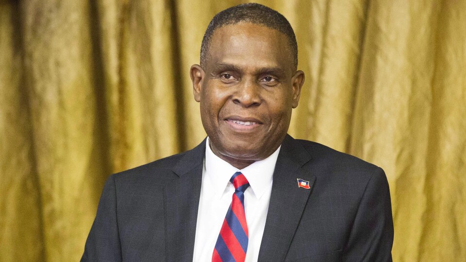 Un homme en complet veston et cravate porte une épinglette aux couleurs d'Haïti