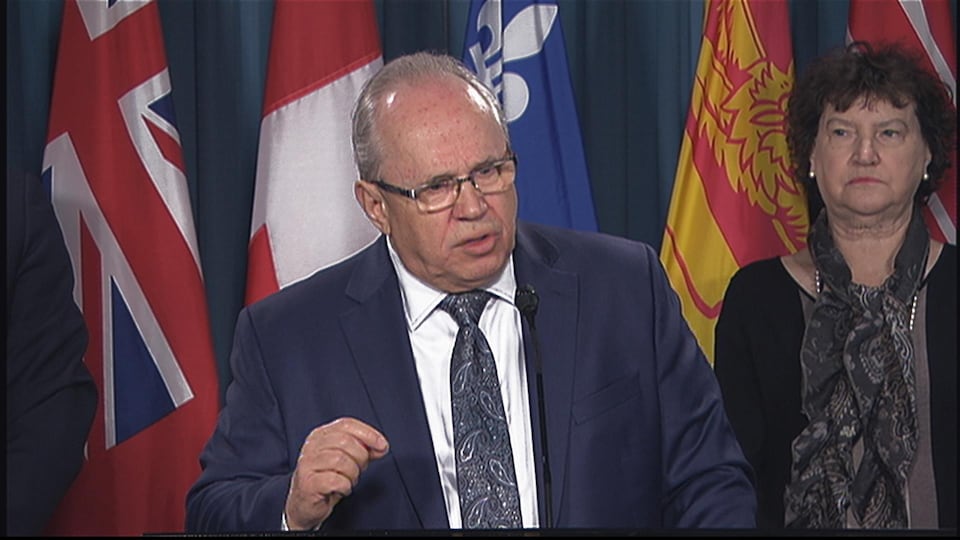 Jean Johnson, le président de la FCFA, est au podium devant les drapeaux du Canada de l'Ontario, du Québec et du Nouveau-Brunswick.