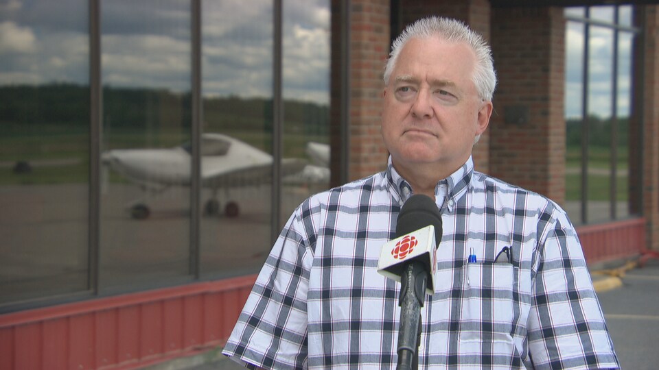 Jean Lessard en entrevue à la caméra de Radio-Canada devant la façade de l'aéroport de Gatineau.