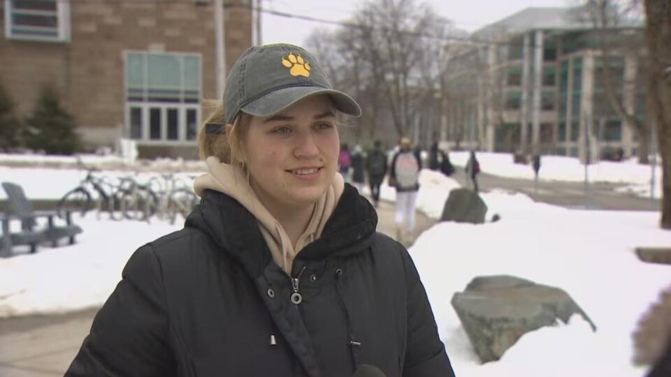 Une femme en entrevue à l'extérieur, sur un campus universitaire.